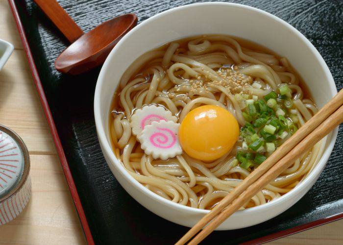 A bowl of Tsukimi udon, featuring noodles in a broth with fish cakes, spring onion and a bright, yellow yolk in the center, representing the moon.